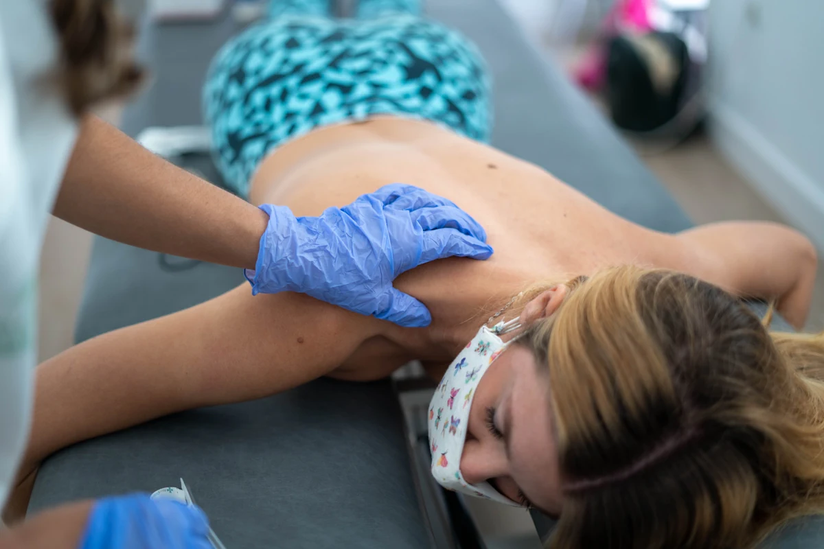 Une femme allongé sur le ventre qui se fait examiner l'épaule